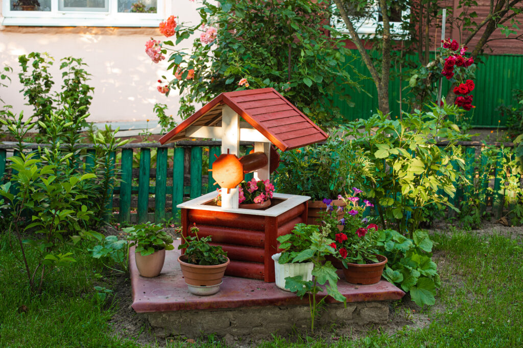 Stock photo of a small garden in the backyard. Fake well with potted flowers. Rustic backyard in countryside or village.